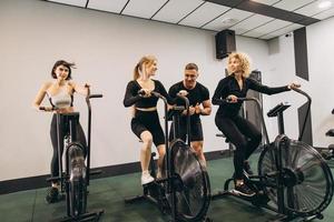 las mujeres jóvenes hacen ejercicio en bicicletas de aire en el gimnasio con entrenador motivador. foto