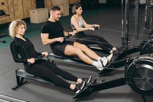 Young man and beautiful women working out with rowing machine at crossfit gym. photo