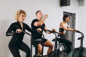 Young man drinking water and women using air bike for cardio workout at cross training gym photo