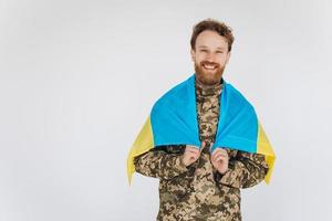 Smiling Ukrainian patriot soldier in military uniform holding a yellow and blue flag on a white background photo