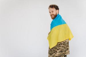 feliz soldado patriota ucraniano con uniforme militar sosteniendo una bandera amarilla y azul en un fondo blanco foto