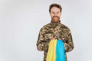 Smiling Ukrainian patriot soldier in military uniform holding a yellow and blue flag on a white background photo