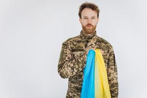 Ukrainian patriot soldier in military uniform holds a hand on a heart with a yellow and blue flag on a white background photo