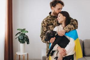 A Ukrainian couple, a soldier in military uniform and a girl wrapped in a Ukrainian flag hold a dog in their arms, happy together. photo