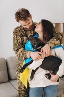 A Ukrainian couple, a soldier in military uniform and a girl wrapped in a Ukrainian flag hold a dog in their arms, happy together. photo