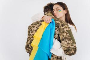 A Ukrainian girl hugs and holds a yellow and blue flag of a military man in uniform and says goodbye to him. photo