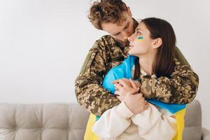 Ukrainian couple, military man in uniform hugs and wraps his wife in the Ukrainian flag. The concept of patriotism. photo