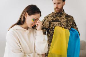 A Ukrainian woman mourns and says goodbye to her military husband in a uniform holding a Ukrainian flag at home photo