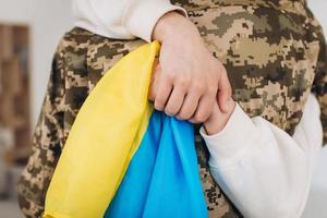 A Ukrainian girl hugs and holds a yellow and blue flag of a military man in uniform and says goodbye to him. photo