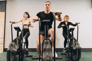 hombre joven y mujer usando bicicleta de aire para entrenamiento cardiovascular en el gimnasio de entrenamiento cruzado foto
