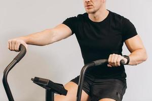 Strong man using air bike for cardio workout at cross training gym. photo