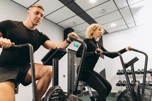 joven y mujer usando bicicleta de aire para hacer ejercicio cardiovascular en el gimnasio de entrenamiento cruzado foto