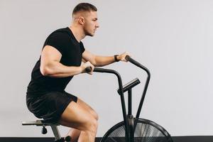 hombre fuerte que usa bicicleta de aire para hacer ejercicio cardiovascular en el gimnasio de entrenamiento cruzado. foto