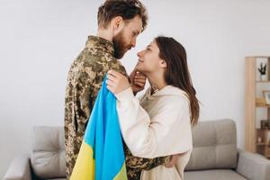 A Ukrainian girl hugs and holds a yellow and blue flag of a military man in uniform and says goodbye to him. photo