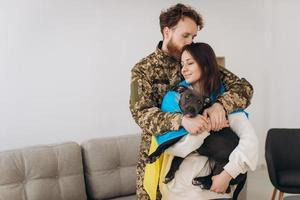 una pareja ucraniana, un soldado con uniforme militar y una niña envuelta en una bandera ucraniana sostienen un perro en sus brazos, felices juntos. foto