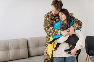 una pareja ucraniana, un soldado con uniforme militar y una niña envuelta en una bandera ucraniana sostienen un perro en sus brazos, felices juntos. foto