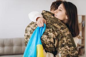 A Ukrainian girl hugs and holds a yellow and blue flag of a military man in uniform and says goodbye to him. photo