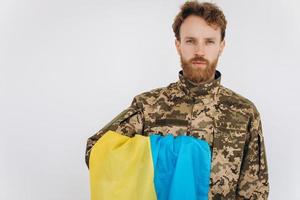 Portrait of an emotional young bearded Ukrainian patriot soldier in military uniform holding a flag in the office photo