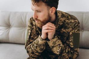 Portrait of emotional young bearded Ukrainian patriot soldier in military uniform sitting on the office sofa photo