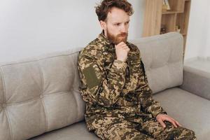 Portrait of emotional young bearded Ukrainian patriot soldier in military uniform sitting on the office sofa photo