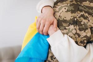 A Ukrainian girl hugs and holds a yellow and blue flag of a military man in uniform and says goodbye to him. photo