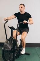 hombre fuerte que usa bicicleta de aire para hacer ejercicio cardiovascular en el gimnasio de entrenamiento cruzado. foto