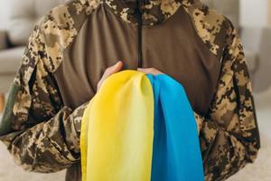 Portrait of an emotional young bearded Ukrainian patriot soldier in military uniform holding a flag standing on his knees photo