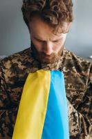 Ukrainian patriot soldier in military uniform holding a yellow and blue flag in the office photo