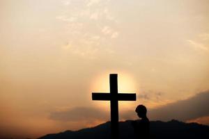 silueta de un hombre rezando frente a la cruz en la montaña al atardecer. concepto de religión. foto