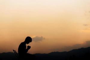 silueta de un hombre tomándose de la mano y rezando en la montaña al atardecer. concepto de religión. foto