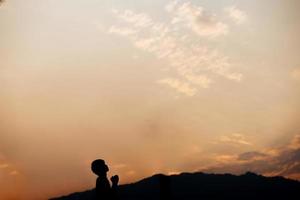 silueta de un hombre rezando en la montaña al atardecer. concepto de religión. foto