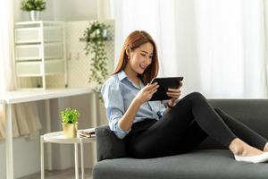 pretty young woman using her digital tablet for reading while sitting on sofa at home. photo