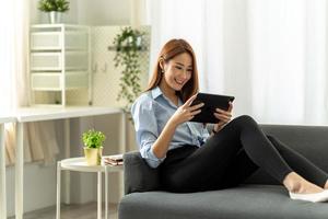 pretty young woman using her digital tablet for reading while sitting on sofa at home. photo