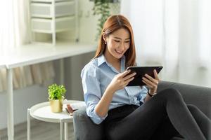 pretty young woman using her digital tablet for reading while sitting on sofa at home. photo