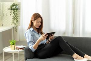 pretty young woman using her digital tablet for reading while sitting on sofa at home. photo