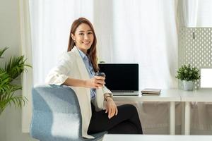 Attractive young brunette asian woman using laptop computer while sitting in a stylish living room. photo