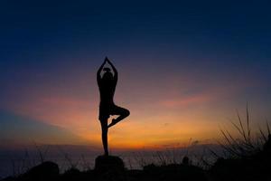 Silhouette of woman practicing warrior one pose yoga on the beach at sunset photo