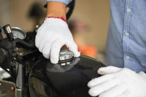 Mechanic repairing motorcycle in workshop garage, Man fixing motorbike in repair shop, Man opening motorcycle fuel tank cap, Repairing and maintenance concepts photo