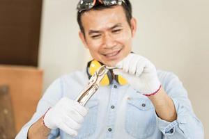 hombre alegre haciendo carpintería en carpintería, carpintero sonriente trabajando con equipo en mesa de madera en taller de madera foto