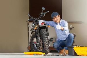 mecánico alegre reparando motocicletas en el garaje del taller, hombre sonriente arreglando motocicletas en el taller de reparaciones, hombre mostrando los pulgares hacia arriba, conceptos de reparación y mantenimiento foto