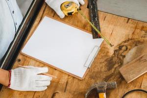 Mockup blank clipboard with white sheet and pencil on carpenter table, Furniture designer holding tape measure planning project at workbench, Man making notes in woodworking shop photo