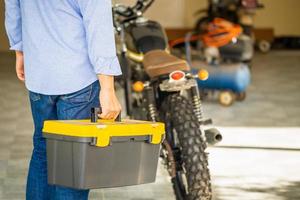 Man carrying toolbox in repair shop, Mechanic repairing motorcycle in workshop garage, Repairing and maintenance concepts photo