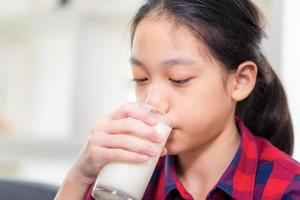 Close up of happy child girl drinks milk, Portrait of Asian little cute kid holding a cup of milk in kitchen photo
