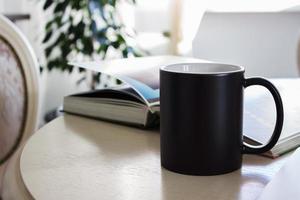 Black mug, cup on a table with book, Mockup photo