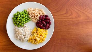 top view of navy bean and red bean and corn and  green peas and millet in white plate on wood background photo