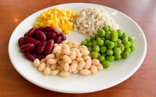top view of navy bean and red bean and corn and  green peas and millet in white plate on wood background photo