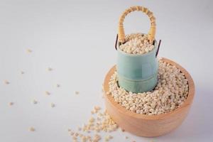 arroz de cebada en taza de madera y cesta de cerámica sobre fondo blanco foto
