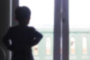 foto borrosa de un niño pequeño parado mirando por la ventana