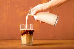 la mano está vertiendo leche en café preparado en estudio con espacio para copiar. foto