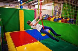 Smiling boy swinging on a rope at indoor playground. photo